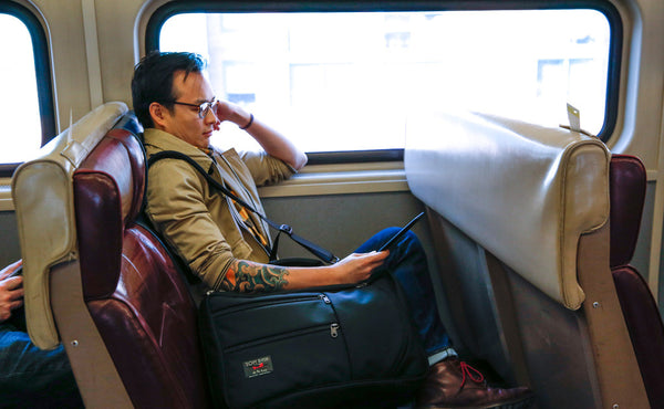 A person sitting in a rail car seat with a Black 525 Ballistic Western Flyer in the seat beside them.